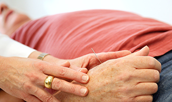 Nahaufnahme einer Hand, in die eine Akupunkturnadel gesetzt wird